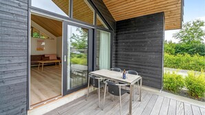 Ein modernes Haus mit einer Holzdiele, einer Essecke mit Tisch und Stühlen sowie einer Glastür, die zu einem Innenraum mit Sofa und Tisch führt.