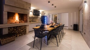 A modern kitchen with a built-in fireplace, a dining area with a long table and chairs, and a TV mounted above the counter. - Gorgeous home in Lovrec with sauna (Lovrec)
