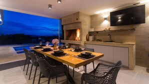 A modern kitchen with a built-in TV, a fireplace, and a dining area with a pool view. - Gorgeous home in Lovrec with sauna (Lovrec)