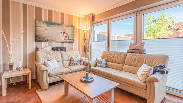 Ein Wohnzimmer mit zwei beigen Sofas, einem Holztisch und einem Gemälde, das eine Strandansicht zeigt.