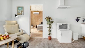 Et moderne køkken med et hvidt køleskab, indbygget ovn og emhætte. Der er en potteplante og et spiseområde med et bord og stole.