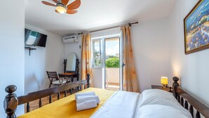 Une chambre d’hôtel comprenant un lit, un bureau avec une chaise, une télévision, un appareil de climatisation et un balcon avec des rideaux.
