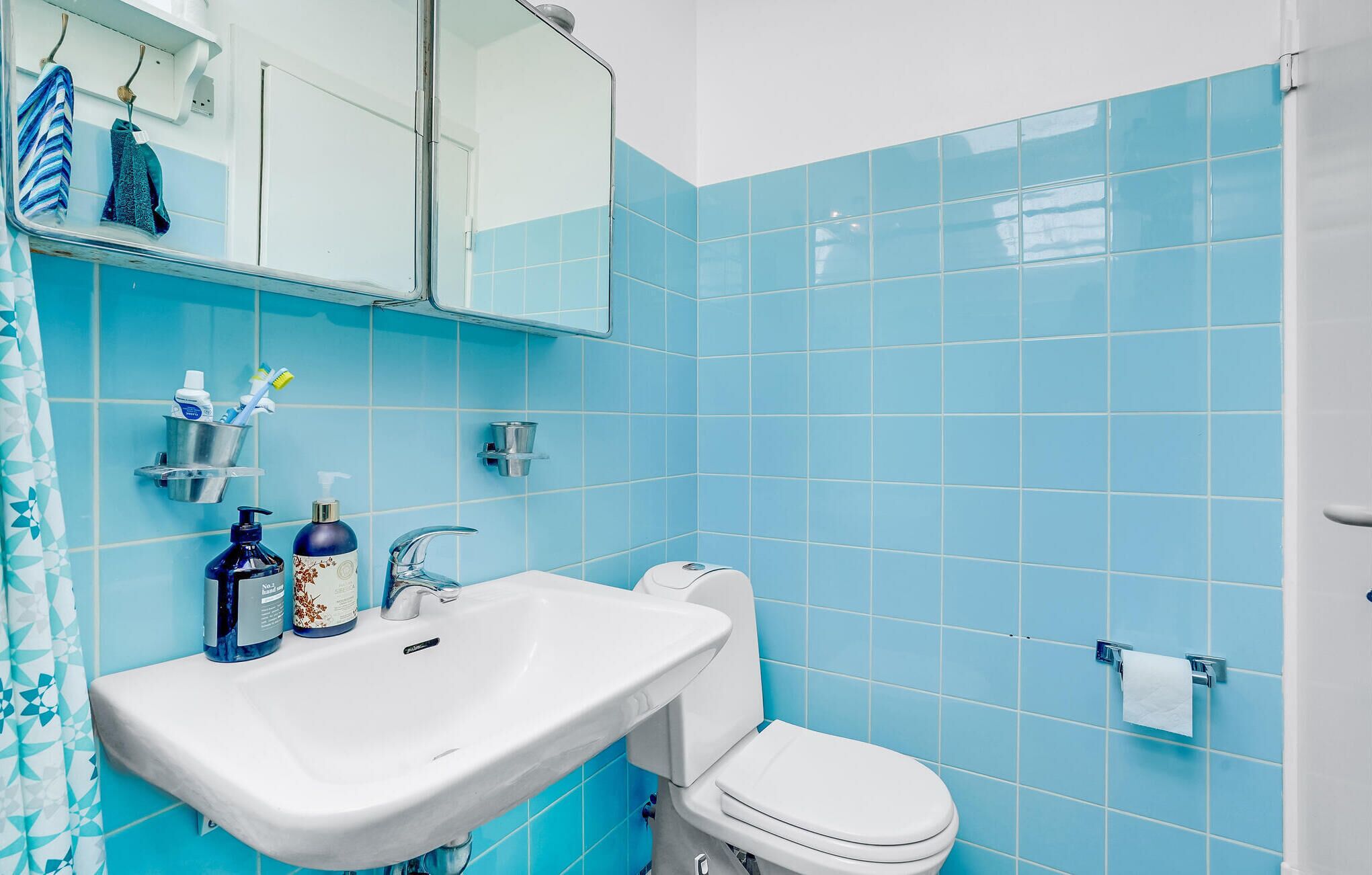 Een badkamer met een wit wastafel, toilet en blauwe betegelde wanden.