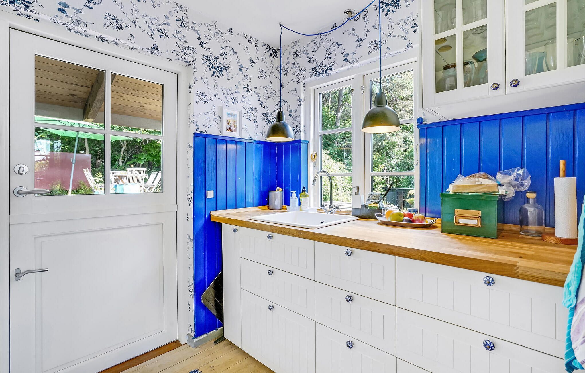 Een keuken met witte kastjes, een houten aanrechtblad en blauwe accenten. Er is een raam met uitzicht op groen.