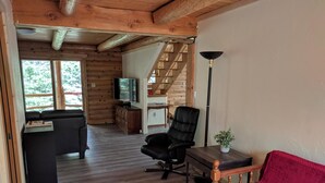 A cozy cabin interior with a wooden floor, a sofa, a chair, a television, and a staircase leading to an upper level. - Spacious cabin in gated community. (Fort Garland)