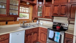 A kitchen with wooden cabinets, a stainless steel sink, a dishwasher, and a stove. - Spacious cabin in gated community. (Fort Garland)