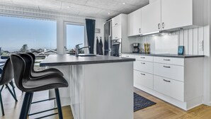Una cucina moderna con mobili bianchi, un'isola centrale con sgabelli da bar, forno integrato e vista sull'esterno.