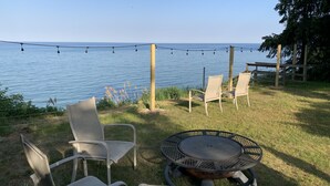Ein grünes Areal im Freien mit einem runden Tisch und zwei Stühlen, mit Blick auf ein Gewässer.