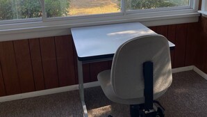 Ein Zimmer mit Schreibtisch und Stuhl, ein großes Fenster mit Blick auf Strand und Meer.