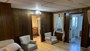 Ein Zimmer mit Holzwandverkleidung, zwei Sesseln, einem Bett mit gemustertem Überwurf und einem Holzboden.