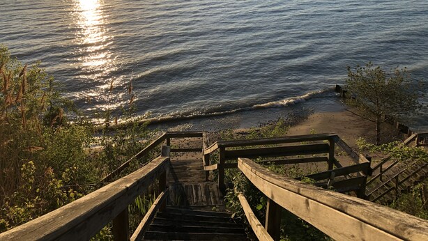 Eine Holztreppe führt zu einem Strand, im Hintergrund das Meer.