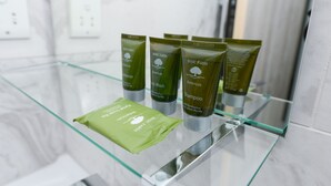 Une salle de bain avec une étagère en verre où sont exposés divers produits de toilette, notamment un savon vert et plusieurs bouteilles de shampoing.