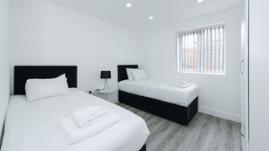 Une chambre d’hôtel moderne avec deux lits, une petite table de chevet avec une lampe, une fenêtre avec des stores et une armoire.