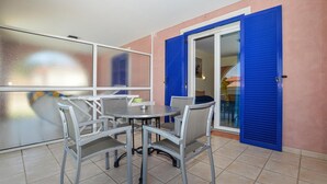 A patio area with a round table and four chairs, a sliding glass door with blue shutters, and a view of the outdoor space.