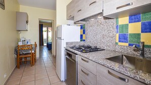 A kitchen with a gas stove, sink, and a refrigerator. There is a dining table with chairs and a window with curtains.