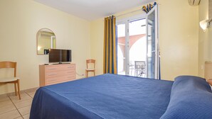 A hotel room with a bed, a dresser, a television, and a balcony with curtains.