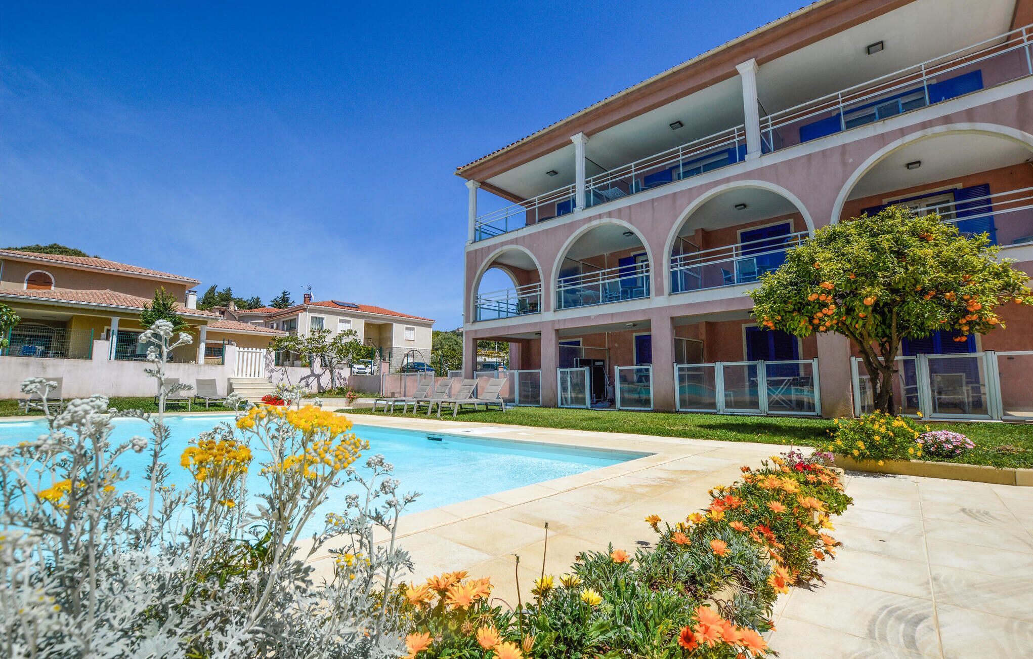 A hotel with a pool, outdoor seating, and a garden with flowers.