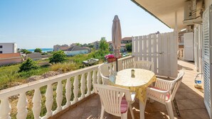 A balcony with a table and chairs, overlooking a coastal area with buildings and greenery. - Amazing apartment in Privlaka with WiFi (Privlaka)