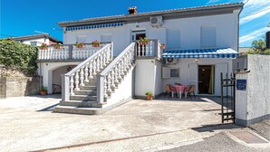 A two-story building with a white facade, a blue awning, and a staircase leading to the upper floor. There is a small outdoor seating area with a table and chairs. - Amazing apartment in Jadranovo with WiFi (Jadranovo)