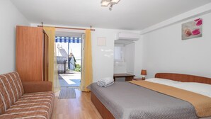 A bedroom with a bed, a wooden headboard, a bedside table with a lamp, a window with curtains, and a view of the outside. - Amazing apartment in Jadranovo with WiFi (Jadranovo)