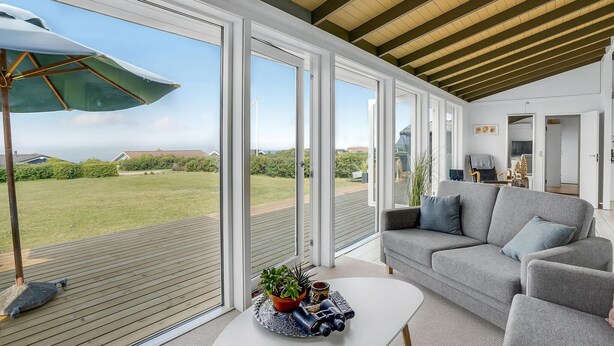 A modern living room with a grey sofa, a coffee table, and a large sliding glass door leading to a wooden deck. - Amazing home in Slagelse with WiFi (Slagelse)