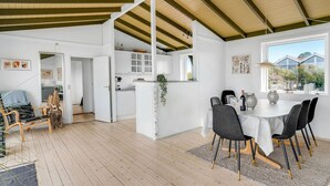 A spacious living area with a wooden floor, a dining table with chairs, and a kitchen area with white cabinets and a hanging plant. - Amazing home in Slagelse with WiFi (Slagelse)