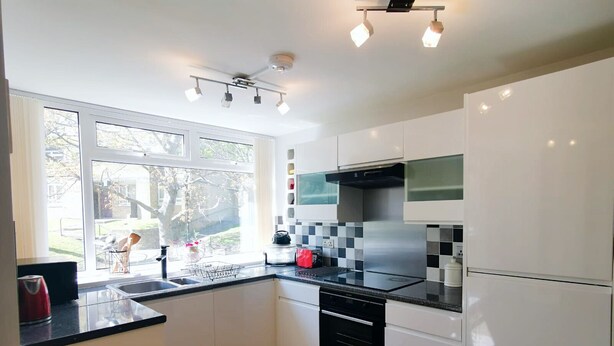 A modern kitchen with white cabinets, a black countertop, a stainless steel range hood, and a window providing a view of the outdoors. - Moorish Castle (Newcastle-upon-Tyne)