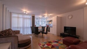 A modern living room with a sofa, a TV, a dining area, and a kitchen in the background. - Moorish Castle (Newcastle-upon-Tyne)
