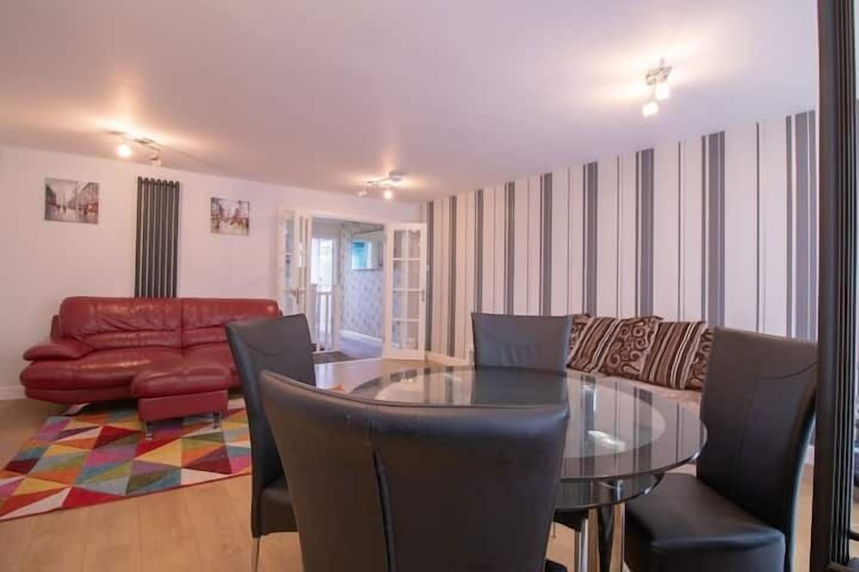 Una sala de estar con un sofá rojo, una mesa de centro de vidrio y papel tapiz a rayas.