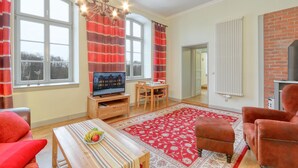 A living room with a TV, a wooden table with fruit, a red patterned rug, and a brick fireplace. - 1 bedroom awesome apartment in Krakow am See (Krakow am See)
