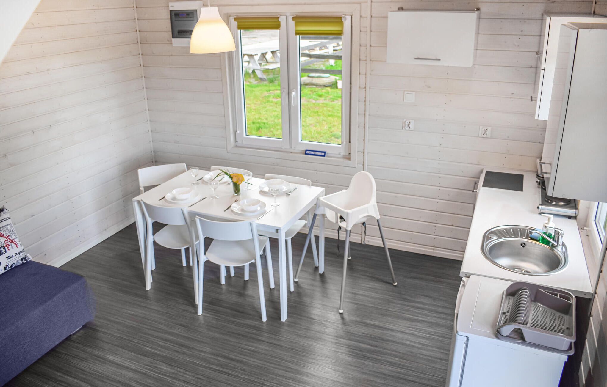Cocina compacta con comedor, muebles blancos, un lavamanos y una ventana con vistas al exterior.