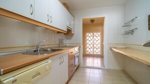 Una cocina con armarios blancos, una encimera de madera, un lavamanos, lavavajillas y suelo de baldosas.