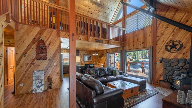 A spacious living room with a large leather sofa, a stone fireplace, and a balcony with wooden railings.