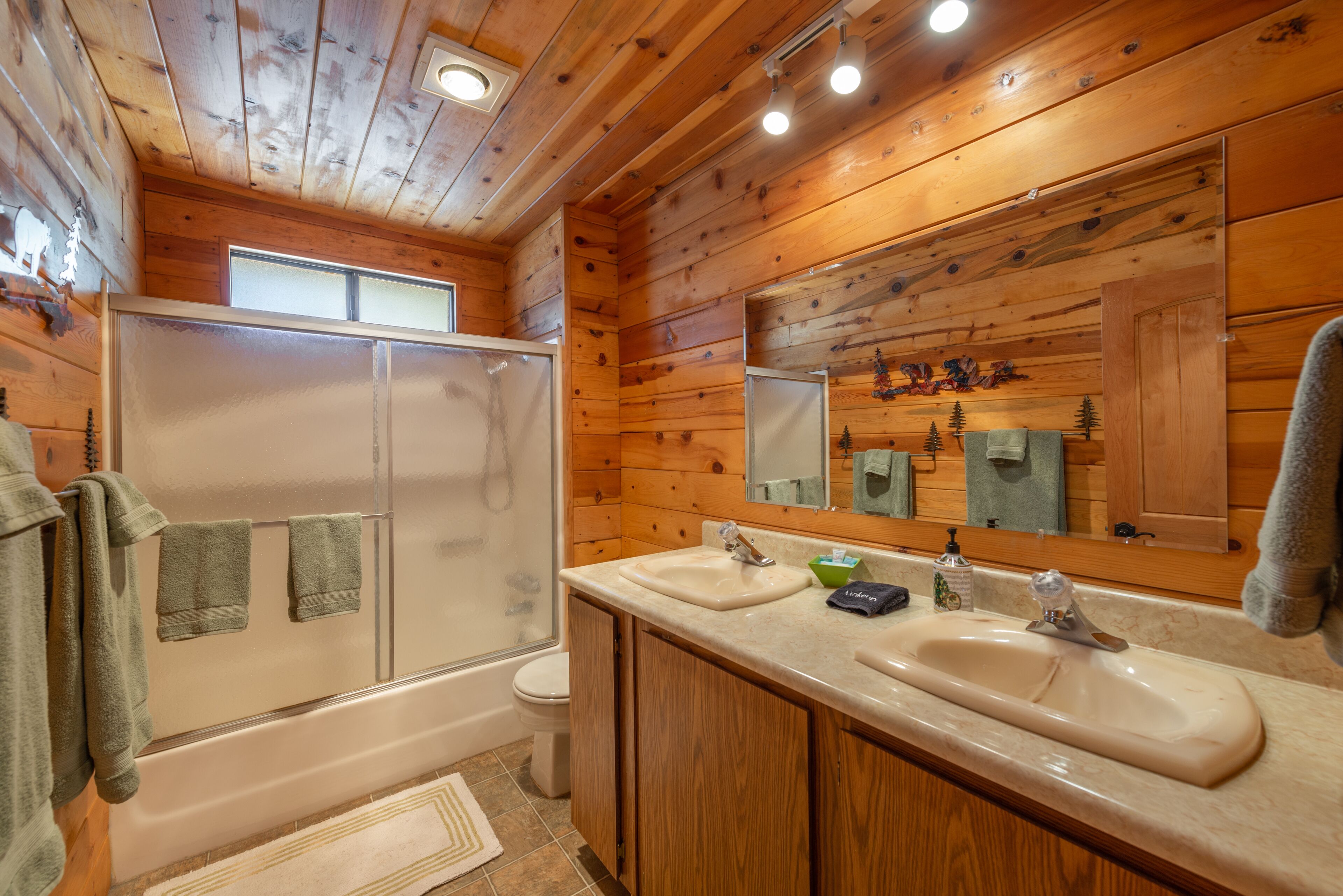 A wooden cabin bathroom with two sinks, a shower, and a toilet.