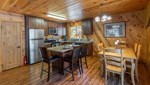 A wooden cabin interior with a kitchen, dining area, and a large window.