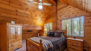 A wooden cabin bedroom with a bed, dresser, nightstand, and a window with blinds.