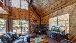 A cozy cabin interior with a stone fireplace, leather furniture, and large windows offering views of the outdoors.