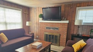 A living room with a brick fireplace, a television mounted above it, and two sofas with cushions. - Cozy cabin-like 2 bedroom home (Reno)