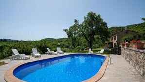 Uma piscina com espreguiçadeiras, cercada por muros de pedra e um edifício de pedra.