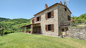 Uma casa de pedra com varanda coberta e muro de pedra.