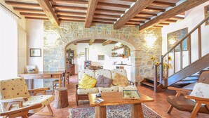 Um interior rústico com paredes de pedra, vigas de madeira, um arco de pedra, um sofá com almofadas estampadas e uma mesa de centro de madeira.