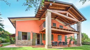 Una casa de dos pisos con balcón, cimientos de piedra y un patio con mobiliario exterior.