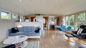 Un espacio habitable moderno y abierto con techo de madera, un sofá gris, una mesa de comedor con sillas azules y un sillón de cuero negro.