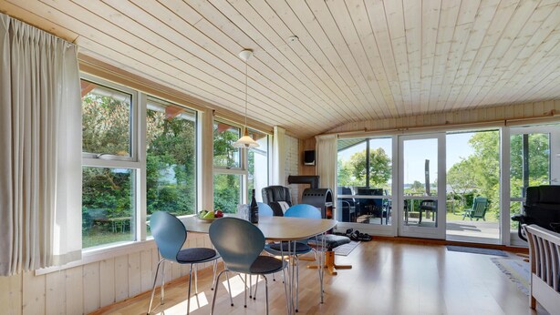 Amplia habitación con techo de madera, ventanas grandes y un comedor con sillas y mesa.