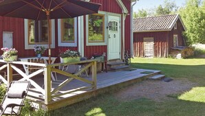 Et rødt træhus med en veranda, et bord med stole og en cykel.