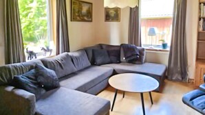 En moderne stue med en grå hjørnesofa, et rundt sofabord og et stort vindue med gardiner.
