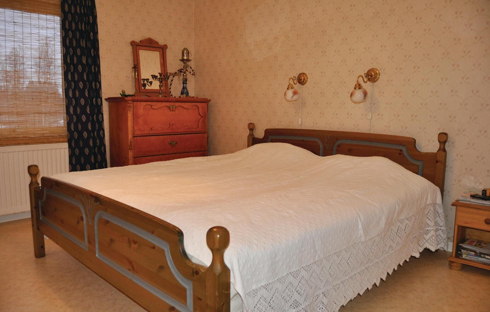 Een slaapkamer met een houten bed, een dressoir, een spiegel en wandlampen.