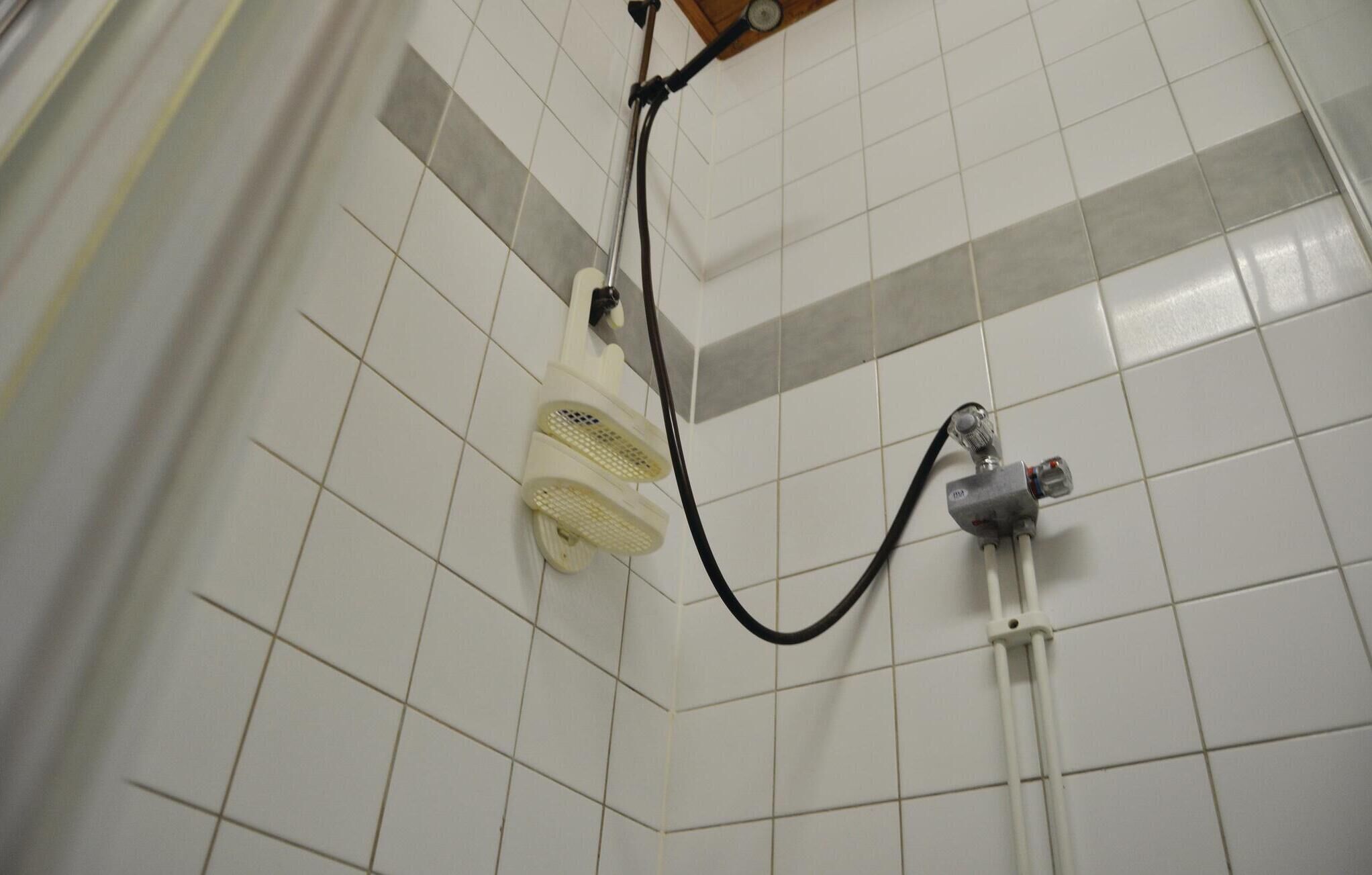 A tiled shower area with a handheld showerhead and a wall-mounted faucet.
