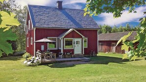 Et rødt træhus med skrå tag, en veranda med udendørs møbler og en cykel parkeret udenfor.