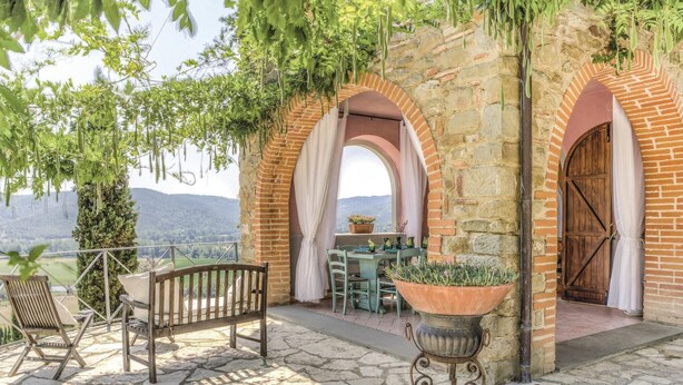 Une terrasse en pierre avec un banc, une table et des chaises, ainsi qu’une plante en pot.